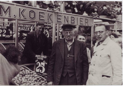 In het midden opa Koek met links twee neven en rechts zijn jongste zoon Marinus. Dit is niet de kraam van opa Koek kraam maar die van zijn zoon. Het is echter wel de enige foto waar hij enigszins herkenbaar op staat met sigaar en pet. <br />Foto: 1953, collectie Jan Wiebenga. 