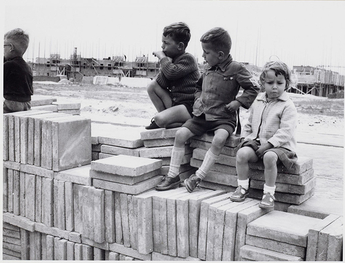  //Kinderen, zittend op trottoirtegels, bij de bouw van de Tuinstad Geuzenveld 1956. Ruys de Beerenbrouckstraat. <br />© Collectie De Arbeiderspers, rechthebbende: AD// 