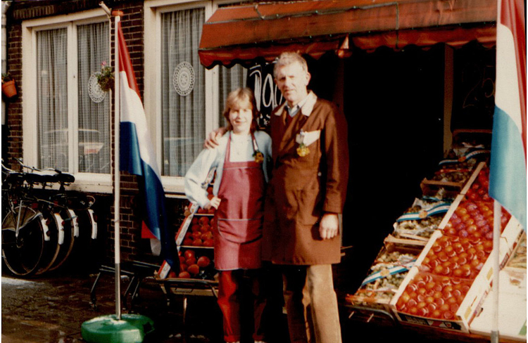  Trotse Kees met een van zijn dochters tussen de jubileumvlaggen. Op de achtergrond de ramen van hun keuken en woonkamer. <br />Foto: 25 november 1985, collectie familie Schouten. 